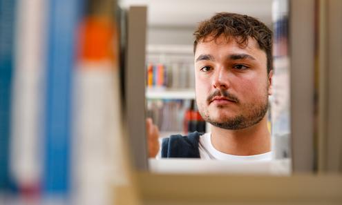 Männlicher Studierender nimmt ein Buch aus einem Bücherregal
