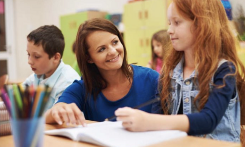 Lehrerin kniet neben Schülerin im Volksschulalter in einer Schulklasse