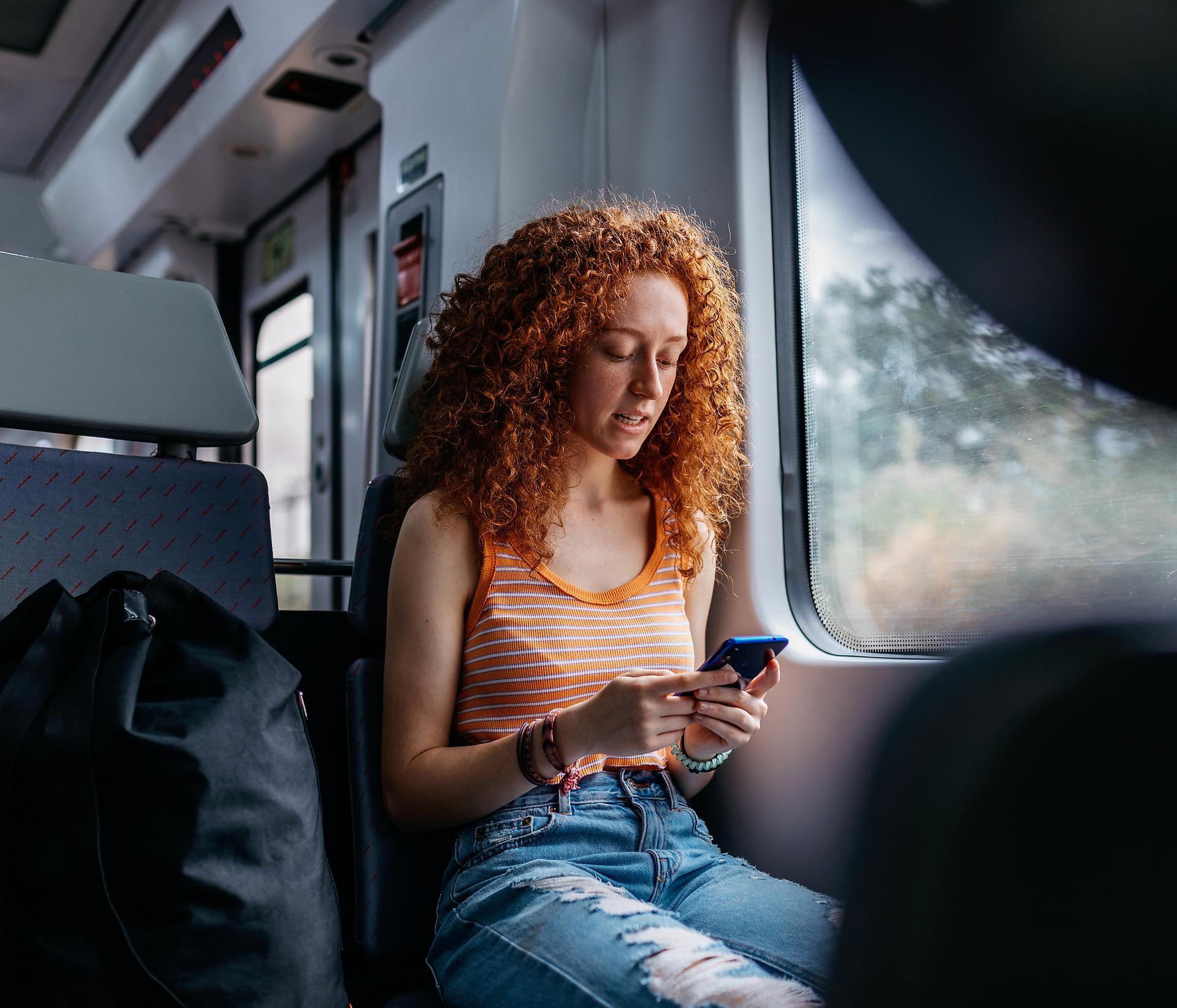 Interessierte junge Frau, die während einer Zugfahrt auf ihr Handy schautltelefon-sendet-