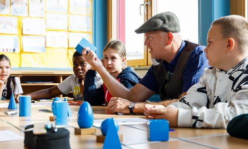 Lehrer mit Schülerinnen und Schülern am Tisch sitzend.